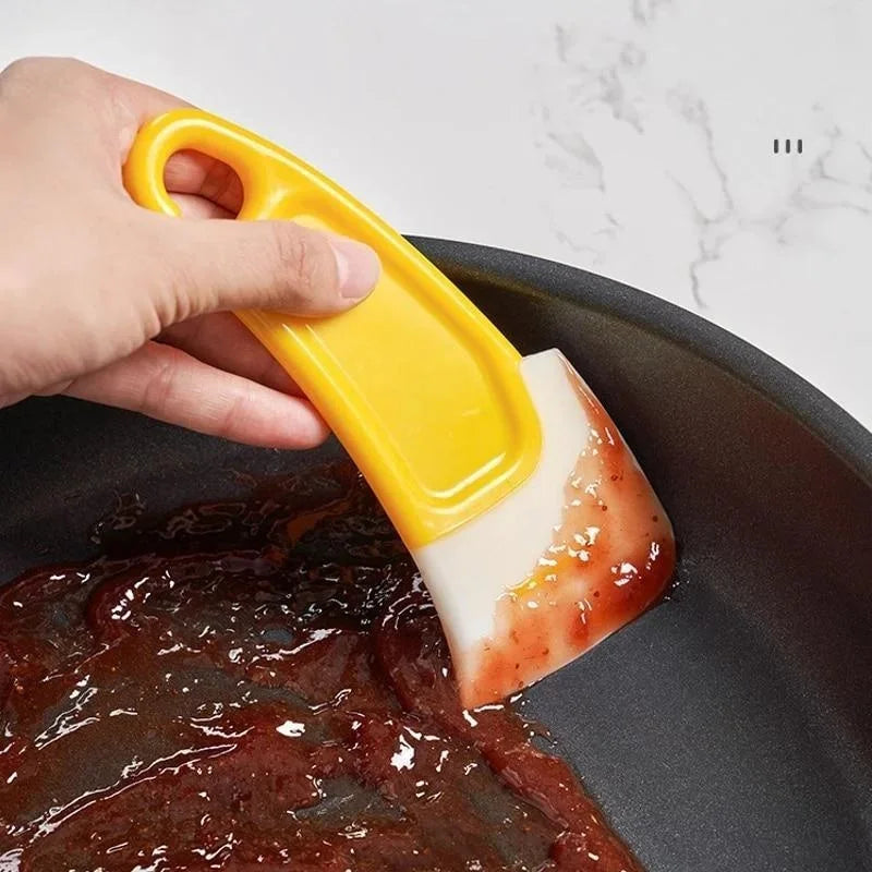 Person using a yellow and white scrubber to clean a frying pan with food residue.
